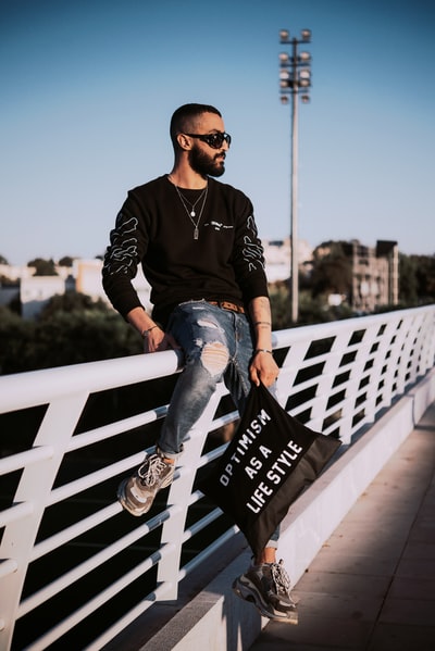 Dressed in a black and white long sleeve shirt and blue denim jeans man sitting on the white wooden seats
